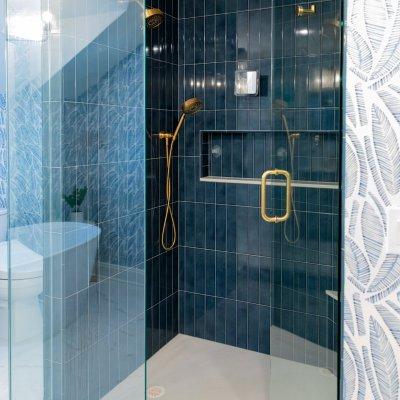 en-suite addition glass door shower with blue tile walls and gold fixtures